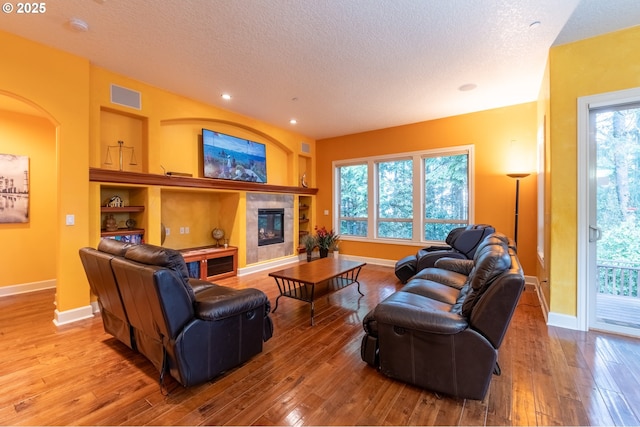 living area featuring a textured ceiling, visible vents, hardwood / wood-style floors, baseboards, and built in shelves