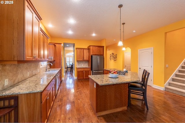 kitchen with a center island, a sink, freestanding refrigerator, brown cabinetry, and decorative backsplash