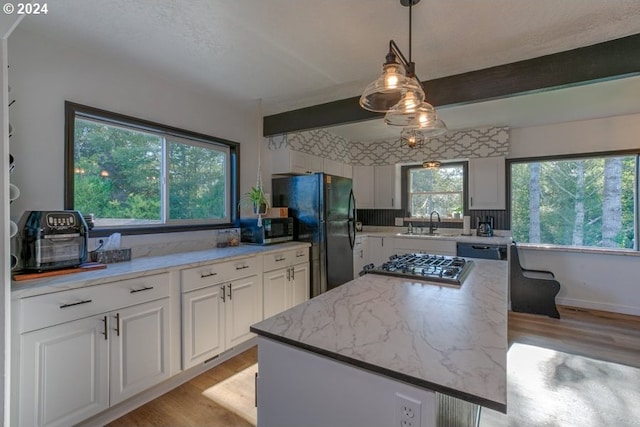 10391041 NE Grant St, Newport, OR 97365 - kitchen featuring appliances with stainless steel finishes, a sink, light wood-style flooring, white cabinets, and beamed ceiling