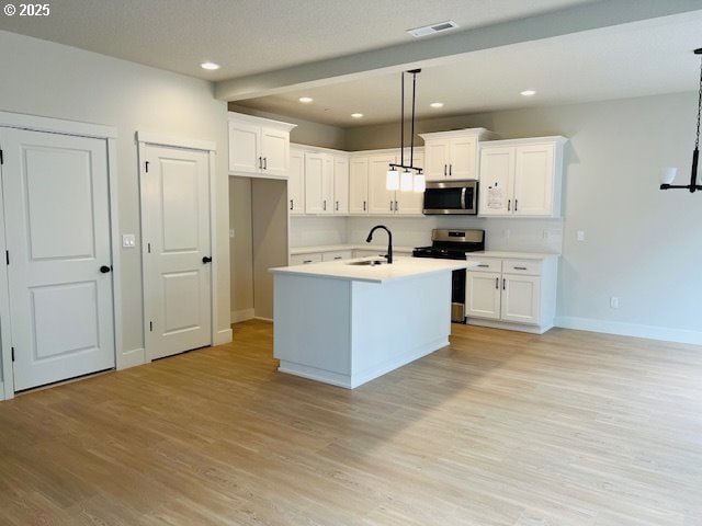 kitchen with hanging light fixtures, appliances with stainless steel finishes, light countertops, and a center island with sink