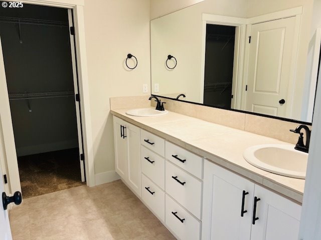 full bath featuring a walk in closet, baseboards, double vanity, and a sink