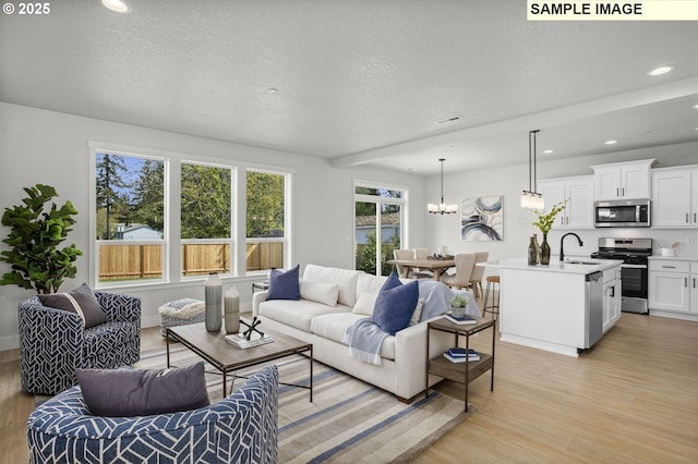 living room with sink, a chandelier, a textured ceiling, and light wood-type flooring