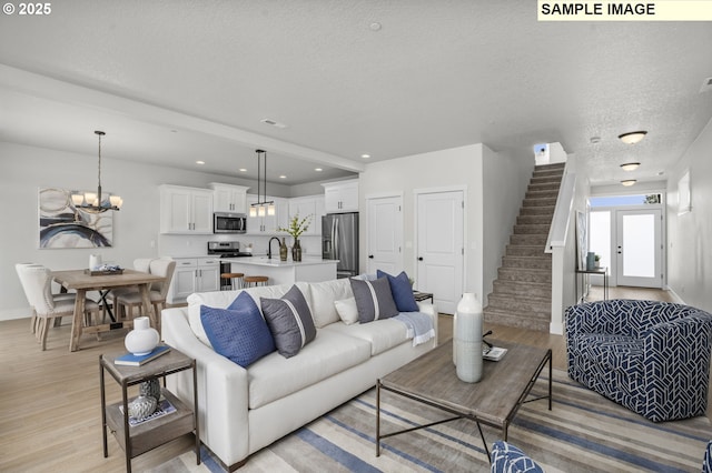 living room with light wood-type flooring, an inviting chandelier, a textured ceiling, and stairway
