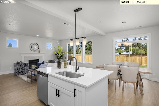 kitchen with light wood-type flooring, dishwasher, a sink, and a glass covered fireplace