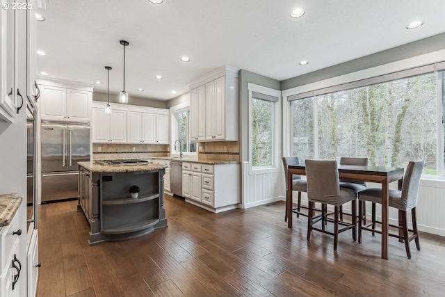 kitchen with stainless steel appliances, light stone counters, a healthy amount of sunlight, and white cabinets