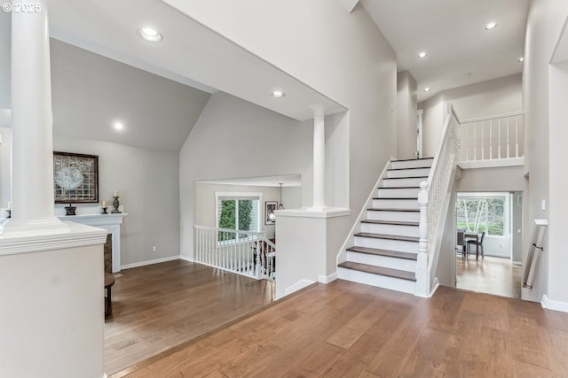 interior space with decorative columns, high vaulted ceiling, and wood finished floors