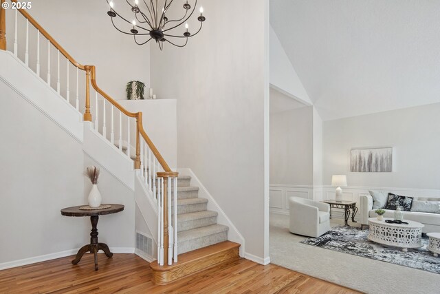 staircase with high vaulted ceiling, hardwood / wood-style flooring, and a notable chandelier