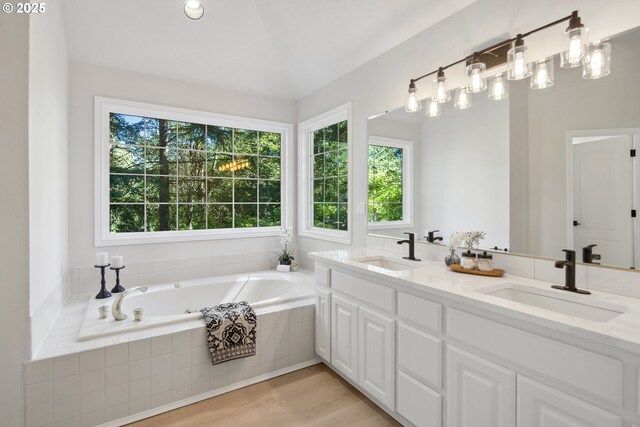 bathroom with tiled tub, vanity, and wood-type flooring