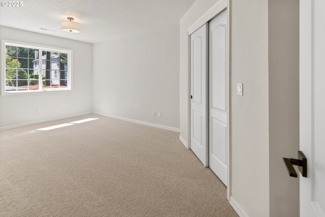 unfurnished bedroom featuring a textured ceiling, light colored carpet, and a closet