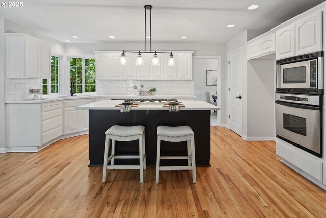 kitchen featuring stainless steel appliances, white cabinetry, light hardwood / wood-style floors, and a center island