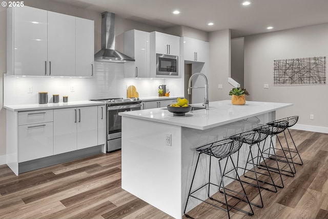 16779 SE Shimmering Leaf St, Happy Valley, OR 97086 - kitchen featuring wall chimney range hood, a kitchen breakfast bar, stainless steel appliances, wood finished floors, and modern cabinets