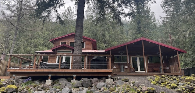 rear view of house featuring metal roof, french doors, a wooden deck, and a view of trees