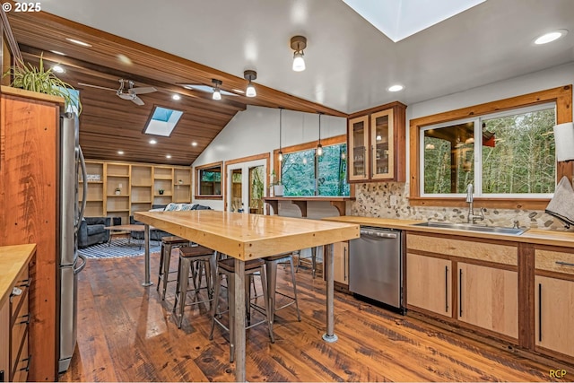 kitchen featuring dark wood-style floors, recessed lighting, a sink, vaulted ceiling with skylight, and appliances with stainless steel finishes