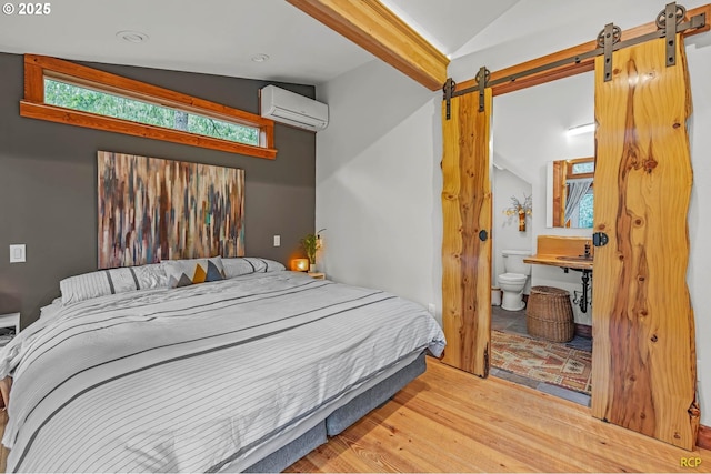 bedroom featuring wood finished floors, a barn door, a wall unit AC, and vaulted ceiling