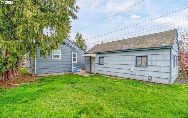 rear view of house featuring entry steps, a lawn, and fence