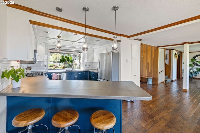 kitchen featuring stainless steel appliances, a peninsula, decorative backsplash, dark wood-type flooring, and ornamental molding