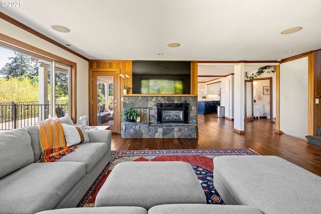 living area with a textured ceiling, a stone fireplace, ornamental molding, and wood finished floors