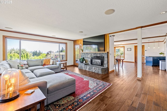 living area with a stone fireplace, a textured ceiling, and crown molding