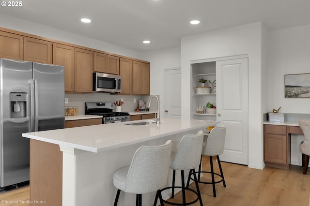 1033 Sommerville Loop, Harrisburg, OR 97446 - kitchen with stainless steel appliances, a sink, brown cabinetry, light wood-style floors, and a kitchen breakfast bar