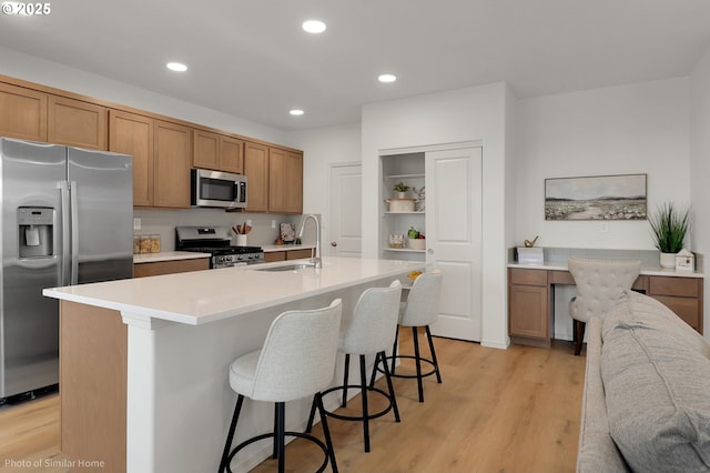 1033 Sommerville Loop, Harrisburg, OR 97446 - kitchen with stainless steel appliances, a sink, light wood-style floors, brown cabinetry, and a kitchen breakfast bar