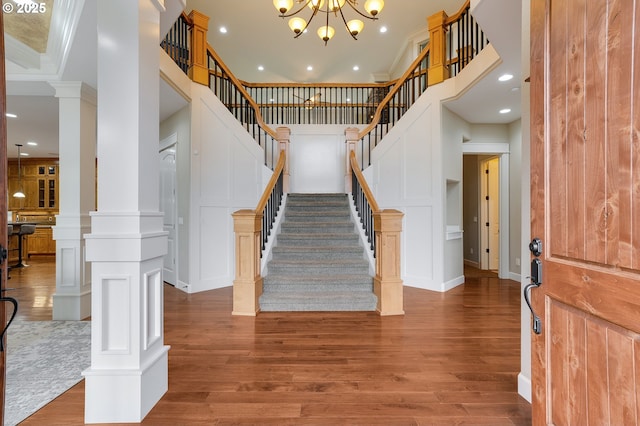 staircase featuring a high ceiling, wood finished floors, crown molding, and ornate columns