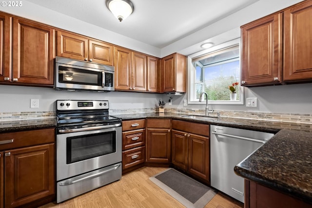 kitchen with appliances with stainless steel finishes, light wood-type flooring, brown cabinets, and a sink