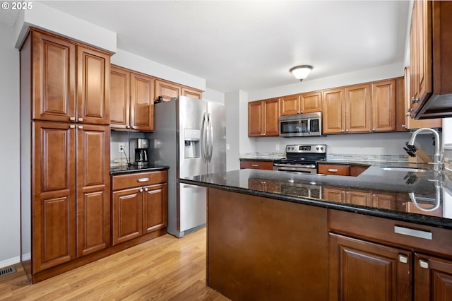 kitchen with appliances with stainless steel finishes, brown cabinetry, dark stone countertops, and a sink