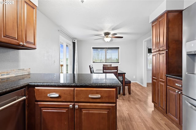 kitchen featuring dark stone counters, ceiling fan, brown cabinets, a peninsula, and light wood-style floors