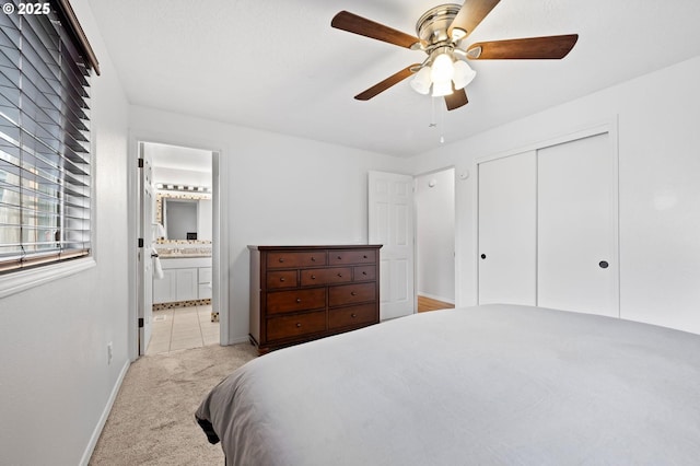 bedroom with a closet, light colored carpet, ensuite bathroom, a ceiling fan, and baseboards