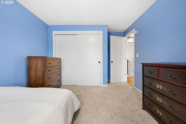 bedroom with baseboards, a closet, and light colored carpet