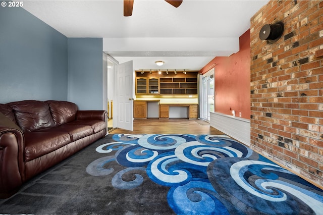 living area featuring brick wall, ceiling fan, wood finished floors, and built in study area