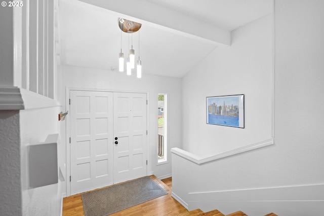 foyer featuring lofted ceiling with beams, baseboards, wood finished floors, and a chandelier