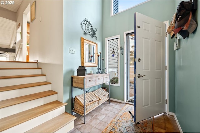 entrance foyer featuring tile patterned flooring, stairs, a towering ceiling, and baseboards