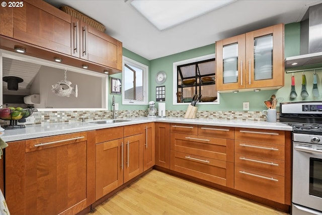 kitchen featuring a sink, light wood-style floors, stainless steel range with gas stovetop, light countertops, and tasteful backsplash