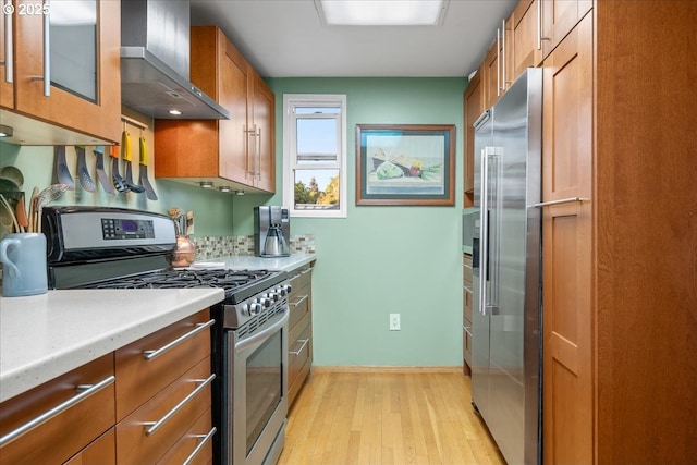 kitchen with light wood-style floors, light countertops, brown cabinetry, wall chimney exhaust hood, and stainless steel appliances