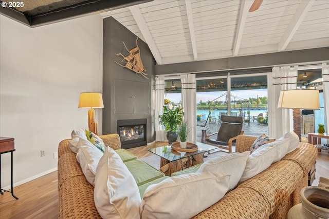 living area featuring a large fireplace, baseboards, lofted ceiling with beams, and wood finished floors