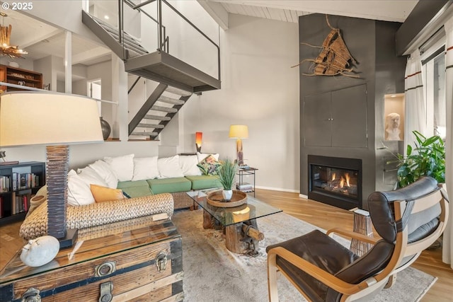 living area with wood finished floors, baseboards, stairway, a large fireplace, and lofted ceiling with beams