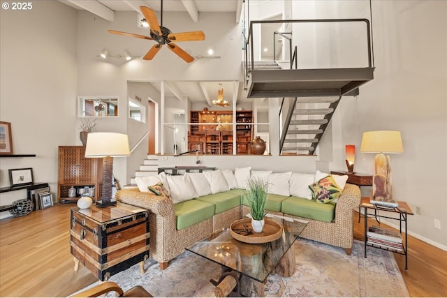 living area with stairs, a towering ceiling, wood finished floors, beam ceiling, and ceiling fan with notable chandelier