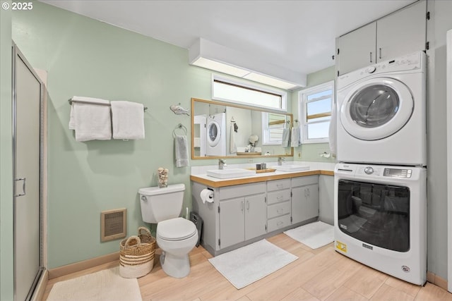 bathroom with toilet, a sink, visible vents, and stacked washer / dryer