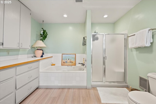 bathroom featuring toilet, a shower stall, wood finished floors, visible vents, and a garden tub