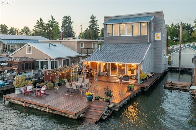back of house featuring outdoor dining area, a deck with water view, and metal roof