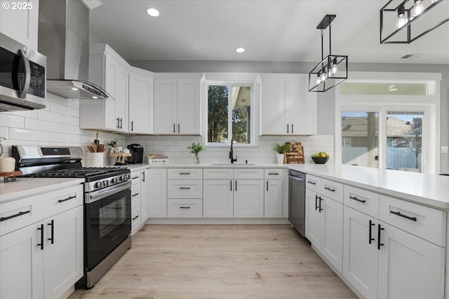 kitchen featuring pendant lighting, white cabinets, appliances with stainless steel finishes, wall chimney exhaust hood, and sink