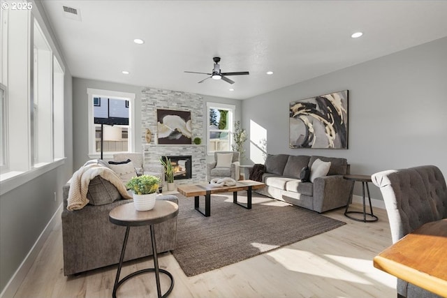 living room featuring ceiling fan, light hardwood / wood-style flooring, and a stone fireplace