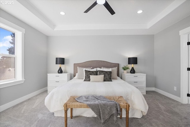 carpeted bedroom featuring multiple windows, ceiling fan, and a raised ceiling