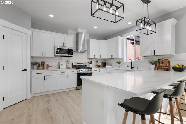 kitchen with stainless steel appliances, white cabinetry, wall chimney exhaust hood, and decorative light fixtures