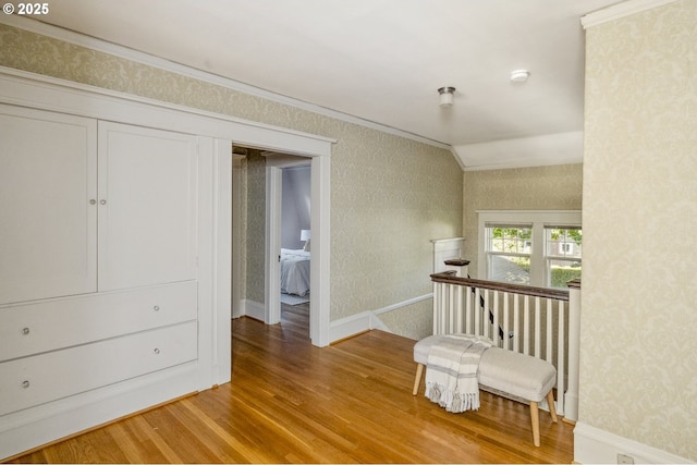 living area featuring wood finished floors, wallpapered walls, crown molding, and baseboards
