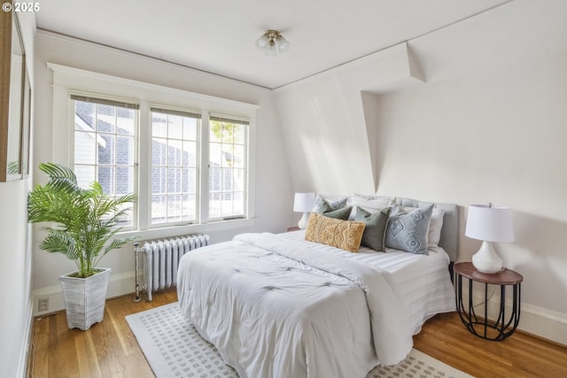 bedroom with radiator heating unit, wood finished floors, and baseboards