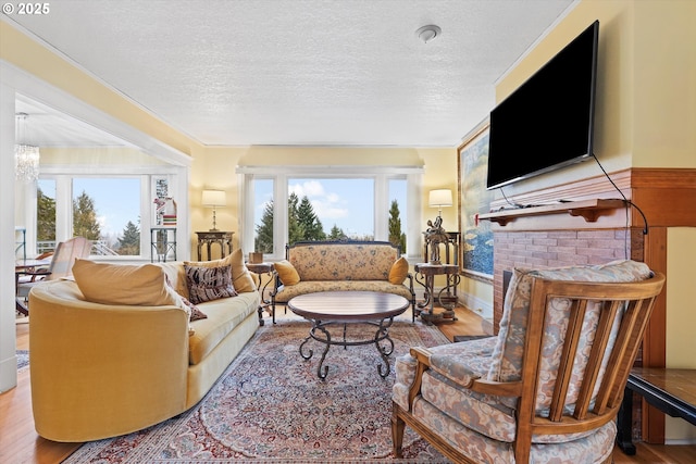 living room featuring a brick fireplace, hardwood / wood-style floors, a textured ceiling, and a notable chandelier