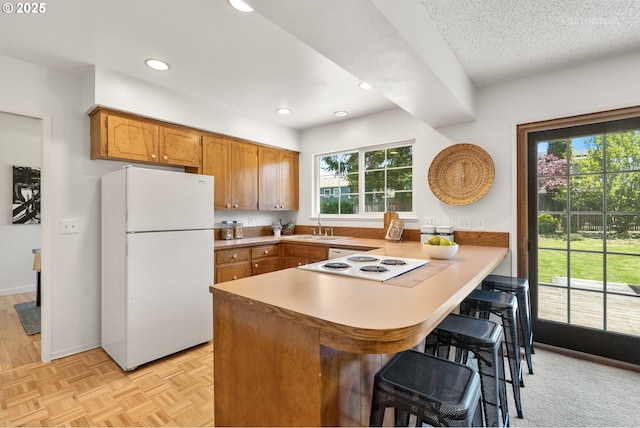 kitchen with white appliances, a peninsula, a sink, brown cabinetry, and a kitchen bar