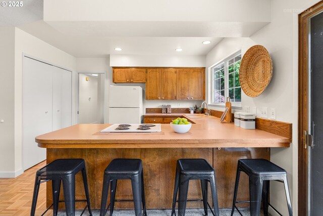 kitchen featuring white appliances, a sink, brown cabinetry, a peninsula, and light countertops